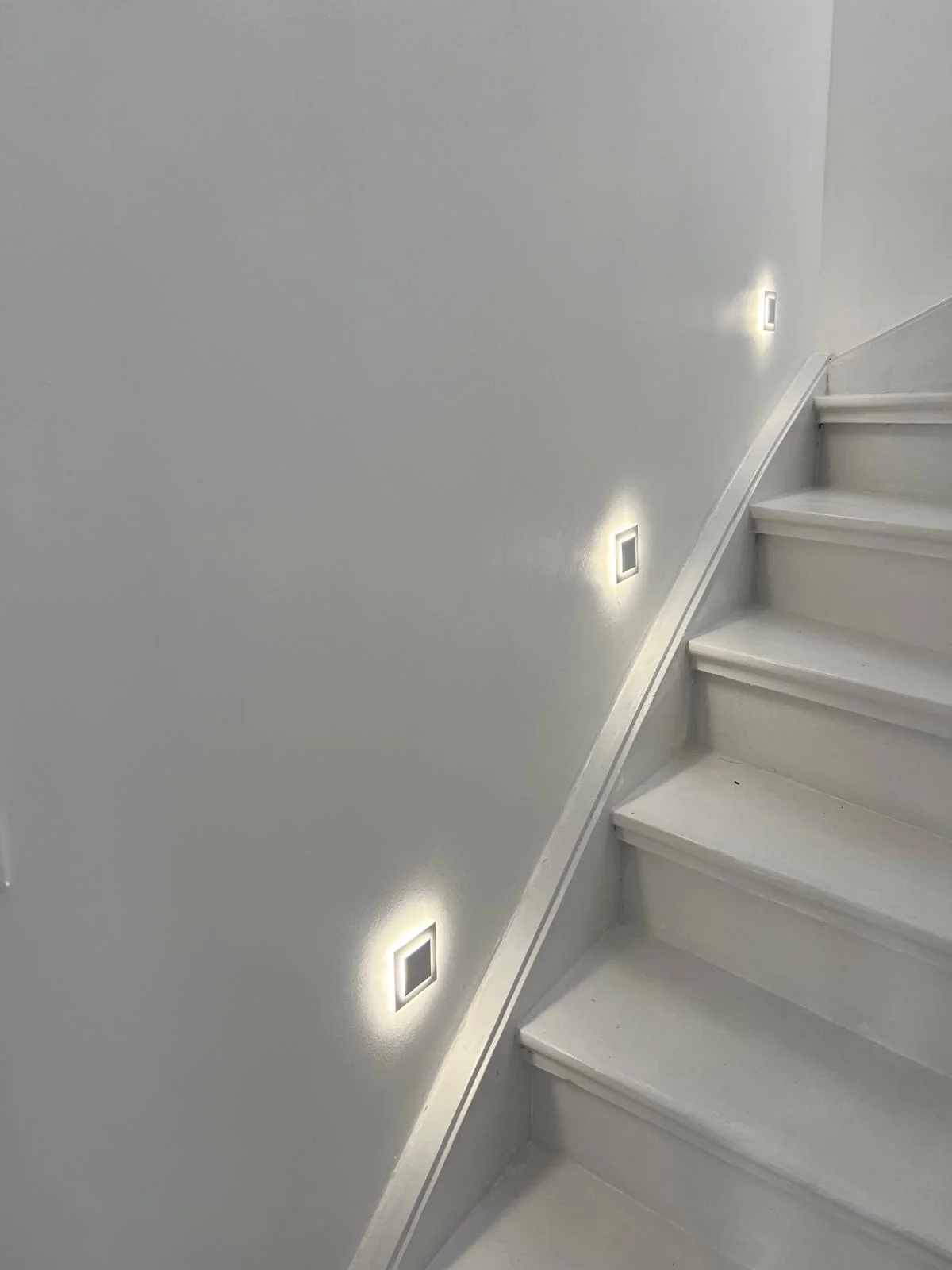 Quadratische LED-Wandleuchten entlang eines hellen Treppenaufgangs